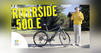 Na pierwszym planie napis: „Riverside 500 E” oraz logo Świat Głuchych MOTO. W tle zdjęcie roweru wraz z prowadzącym odcinek Jakubem Malikiem.